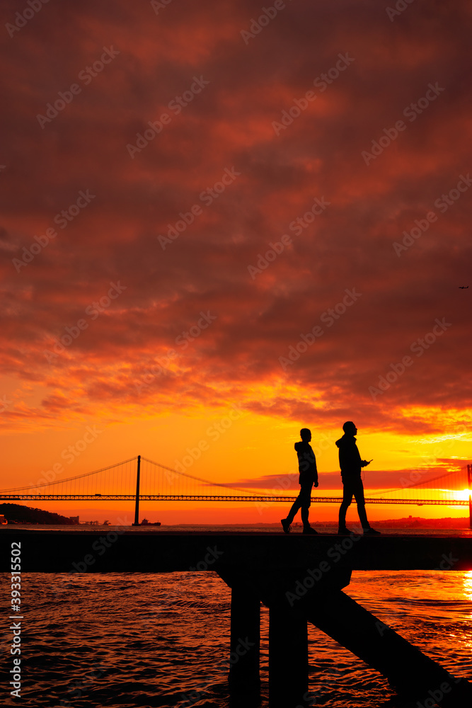 Silhouette of lovers walking with a  bridge in the background sunset time Lisbon