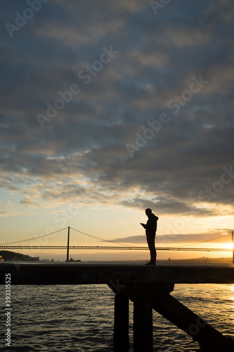 silhouette of a man looking at his phone on a bridge