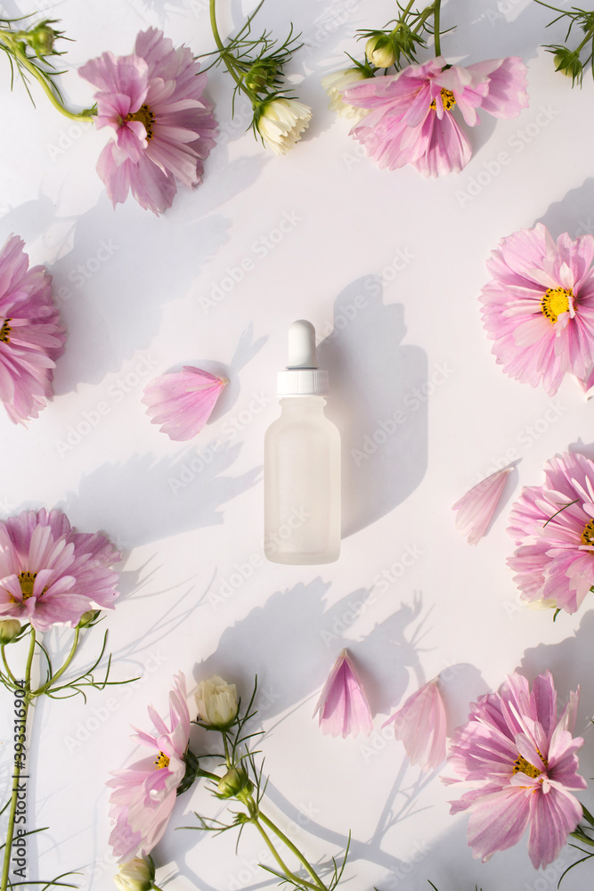 Glass bottle with pipette next to fresh flowers and petals on white background. Natural beauty product. Flat lay, top view. Glass bottle with pipette next to fresh flowers and petals on white background. Natural beauty product. Flat lay, top view.