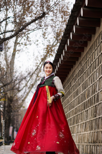 A beautiful asian woman wearing a traditional dress or Hanbok is turning and posing beside a castle wall with a winter background in Seoul, South 