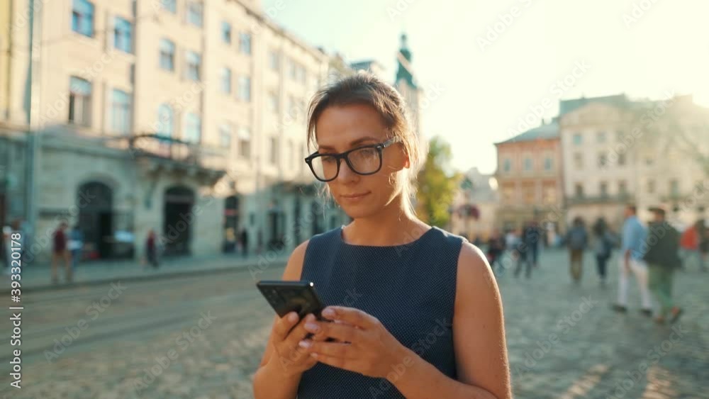 Woman walking down an old street and using smartphone at sunset. Slow motion.