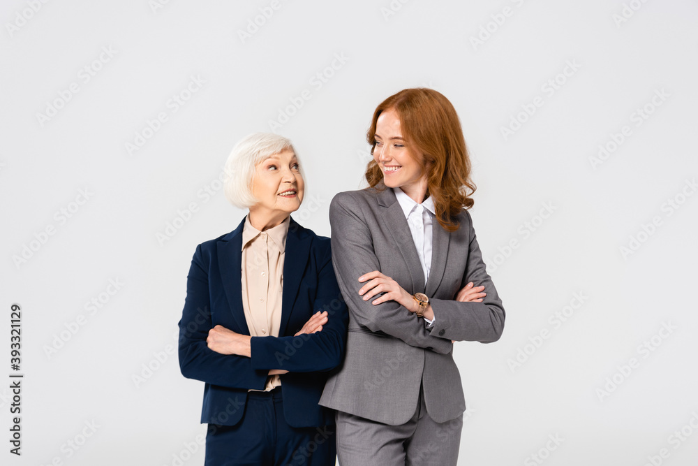 Businesswoman looking at senior colleague with crossed arms isolated on grey