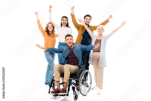 Cheerful multiethnic friends standing near man in wheelchair on white background