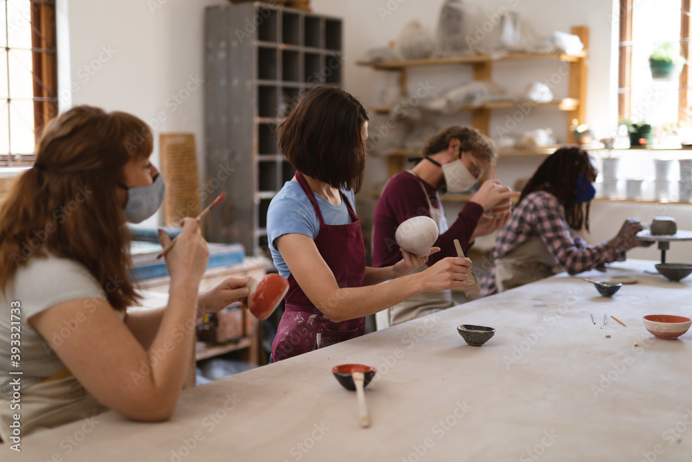 Multi-ethnic group of potters in face masks working in pottery studio Multi-ethnic group of potters in face masks working in pottery studio
