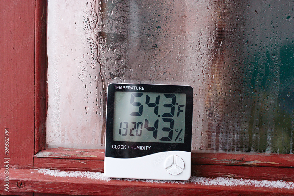 Electronic clock, calendar, thermometer, and hygrometer, against the background of condensation on glass, high humidity. Digital hygrometer in the laboratory shows the temperature of the pharyngeite