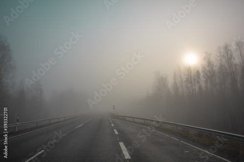 Poor visibility. The road is in heavy fog, along the edges of the road there is a forest. Autumn morning in November. Photo through the windshield of a car