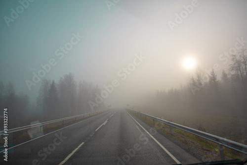 Poor visibility. The road is in heavy fog, along the edges of the road there is a forest. Autumn morning in November. Photo through the windshield of a car