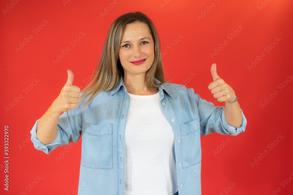 Smiling pretty young woman showing thumbs up isolated on red background Smiling pretty young woman showing thumbs up isolated on red background