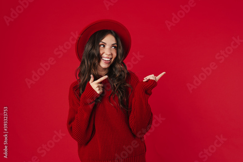 Joyful beautiful girl in hat pointing fingers aside and smiling
