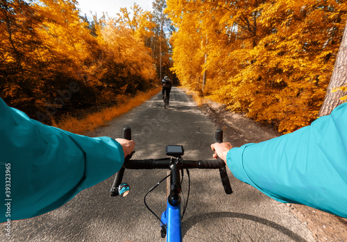 First-person view of a cyclist riding with a friend in the autumn forest with yellow leaves.
