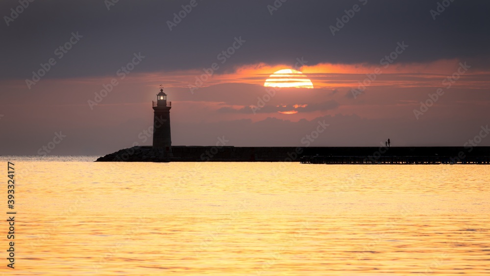 Lighthouse at sunset with large sun, golden sea and people, Andratx, Mallorca, Spain.