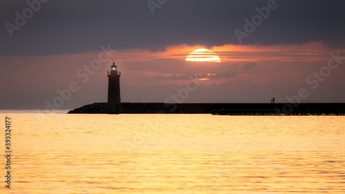 Lighthouse at sunset with large sun, golden sea and people, Andratx, Mallorca, Spain.