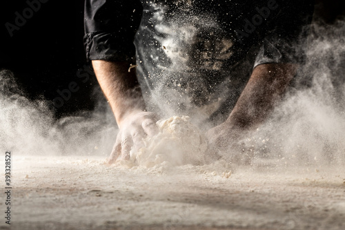 Beautiful and strong men's hands knead the dough from which they will then make bread, pasta or pizza. A cloud of flour flies around like dust. Food concept