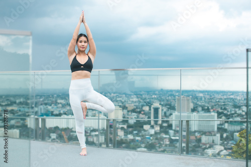 Beautiful asian woman doing a yoga exercise on he rooftop of a skyscraper at sunset.Yoga and meditation in a modern urbanistic city. Young attractive girl .
