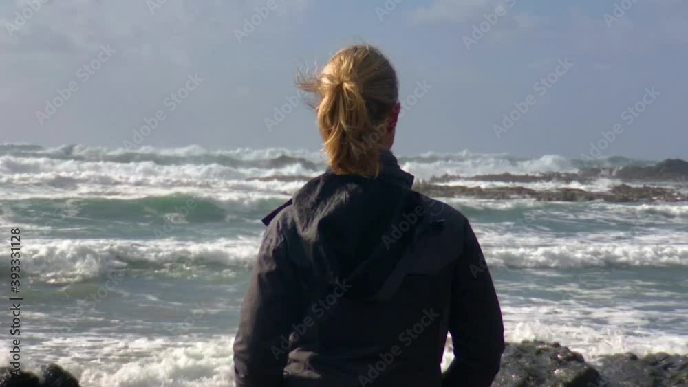 Woman standing on rocky coast, watching restless sea Woman standing on rocky coast, watching restless sea
