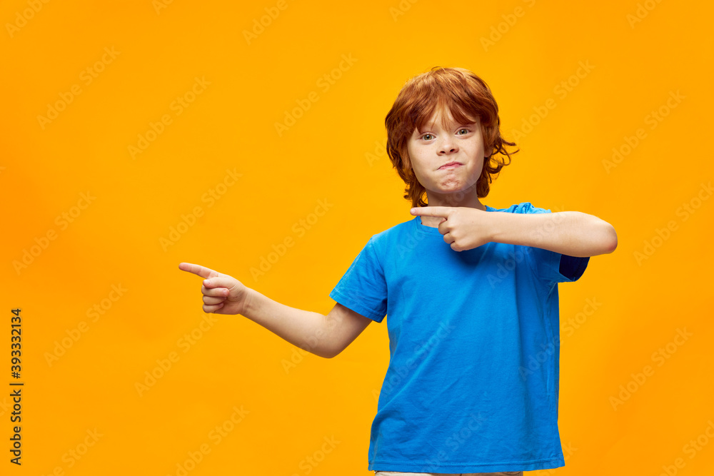 Cheerful red-haired boy gesturing with his hands pointing fingers to the side blue t-shirt Cheerful red-haired boy gesturing with his hands pointing fingers to the side blue t-shirt