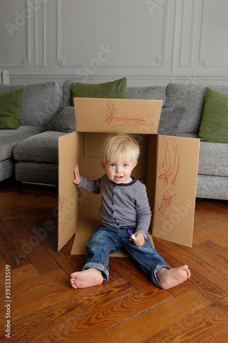 Toddler boy sitting in cardboard box holding marker