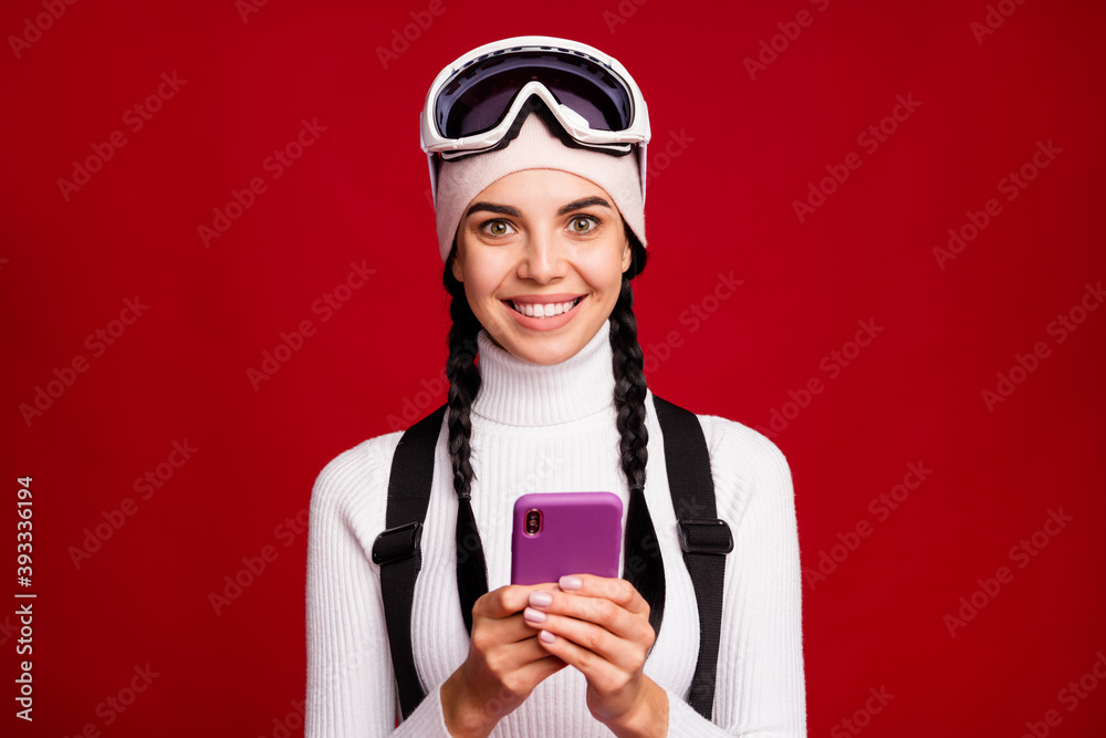Photo of young lovely pretty smiling cheerful girl skier browsing in phone during winter vacation isolated on red color background Photo of young lovely pretty smiling cheerful girl skier browsing in phone during winter vacation isolated on red color background