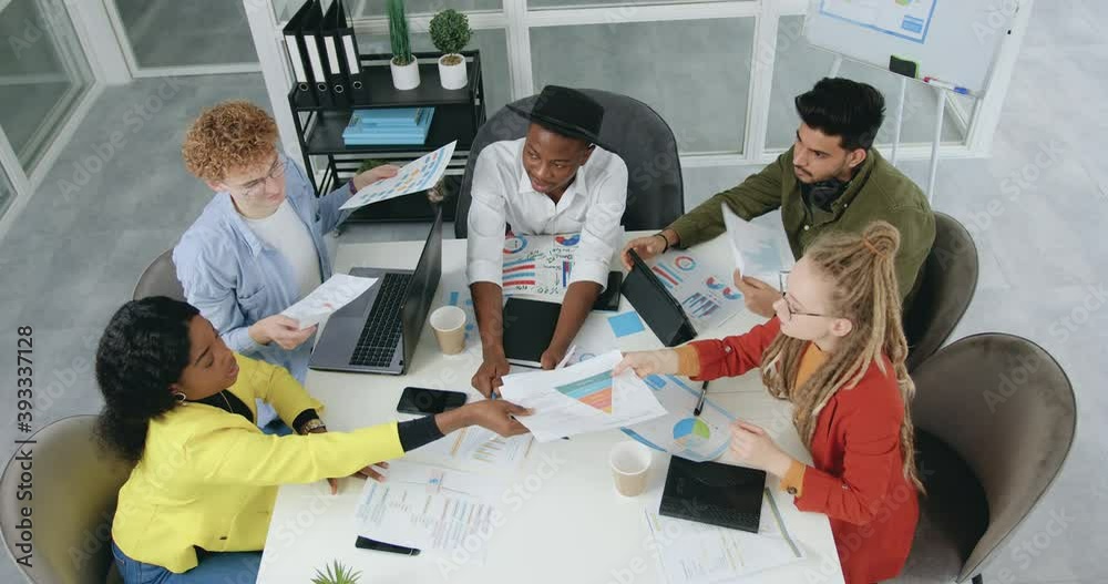 View from top where good-looking professional successful experienced 30s diverse team exchanging with documents while working together in office room