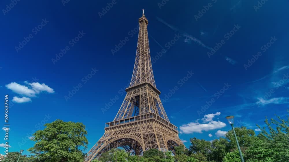 Eiffel Tower from Siene river waterfront in Paris timelapse hyperlapse, France. Blue cloudy sky at summer day with green trees and people walking around