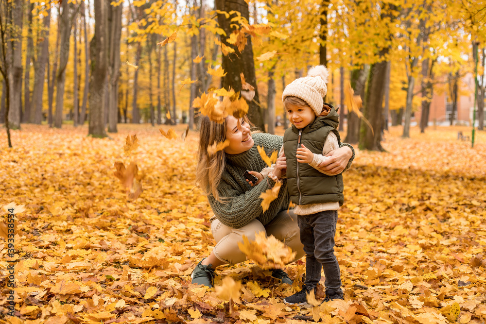 Young Mother with her little son in the autumn park have a fan. Yellow foliage, outdoor time with kids. Independent Happy Single Mother