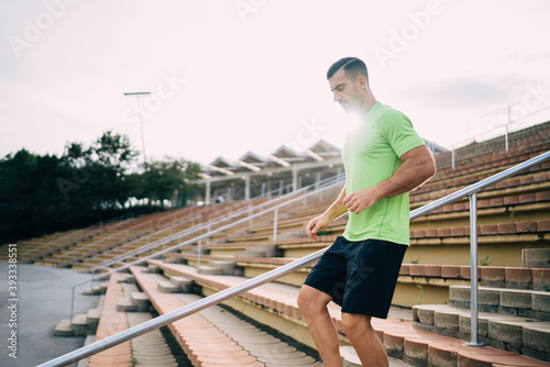 Strong energetic male runner in tracksuit enjoying active and healthy lifestyle have cardio workout for keeping perfect body shape, backlit of Caucasian sportsman training at stadium stairs in morning © BullRun