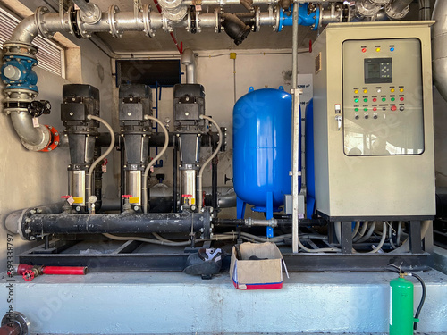 Large water pump room that has been used for a long time. There are three large motors and a control cabinet with green fire extinguishers.