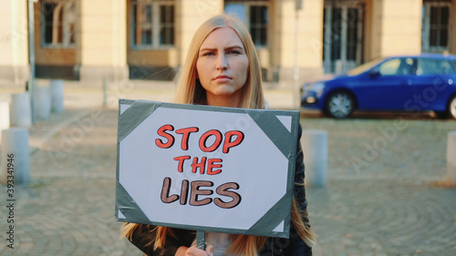Concerned woman with protest banner calling to stop lies by walking on the city street © art24pro