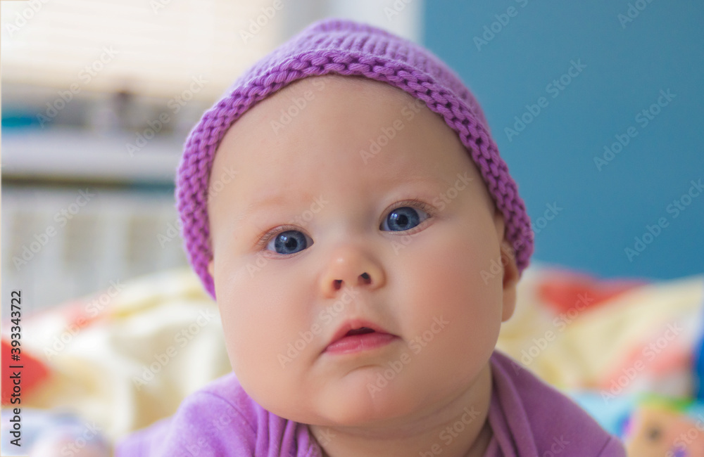 Little baby girl posing in purple bodysuit and knitted hat lying on the bed Little baby girl posing in purple bodysuit and knitted hat lying on the bed