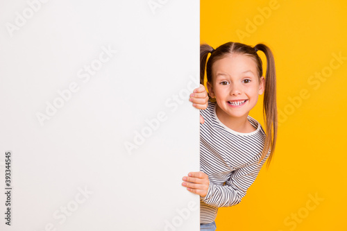 Photo of young happy smiling little girl child kid stand behind white wall isolated on yellow color background