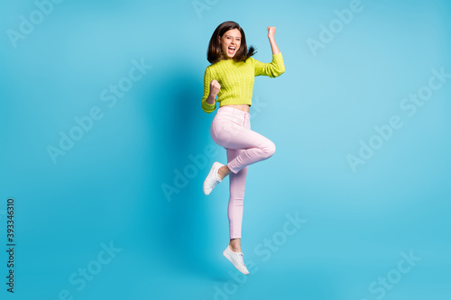 Photo portrait full body view of successful girl celebrating victory with fists in air jumping up isolated on pastel blue colored background