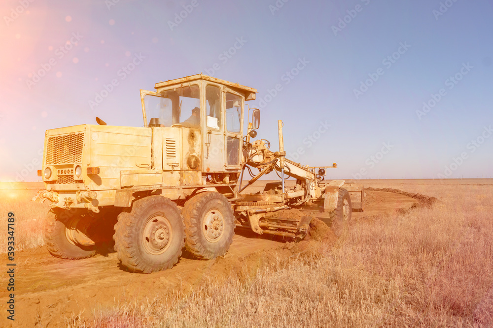 Obraz premium grader machine making a new road, dig the gravel dirt in the field