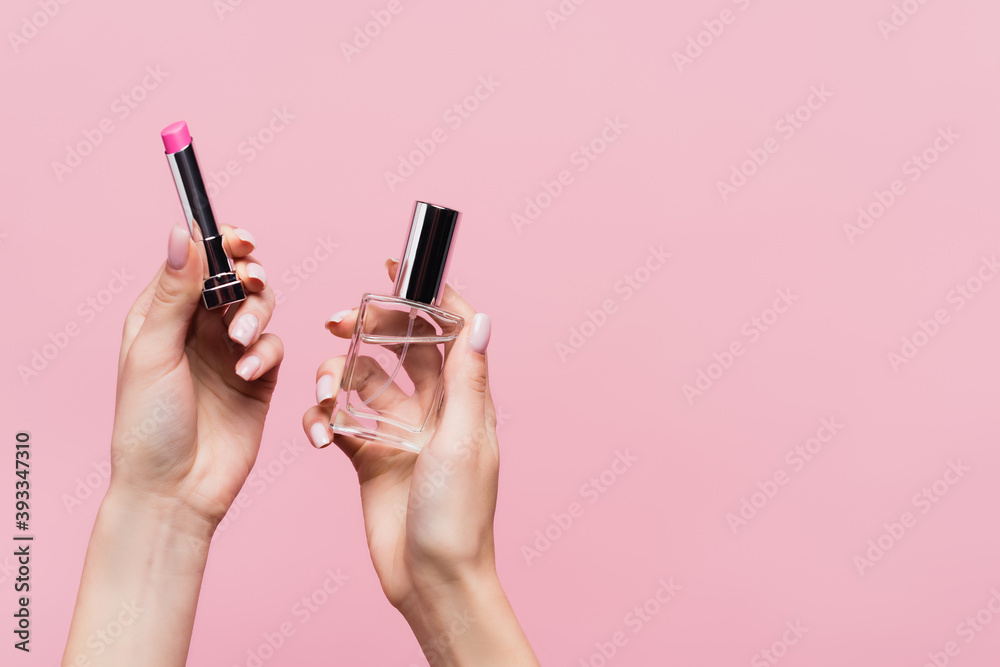 cropped view of woman holding lipstick and bottle with perfume isolated on pink - obrazy, fototapety, plakaty 