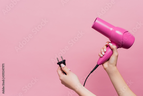 cropped view of woman holding cable with plug and hair dryer isolated on pink photo