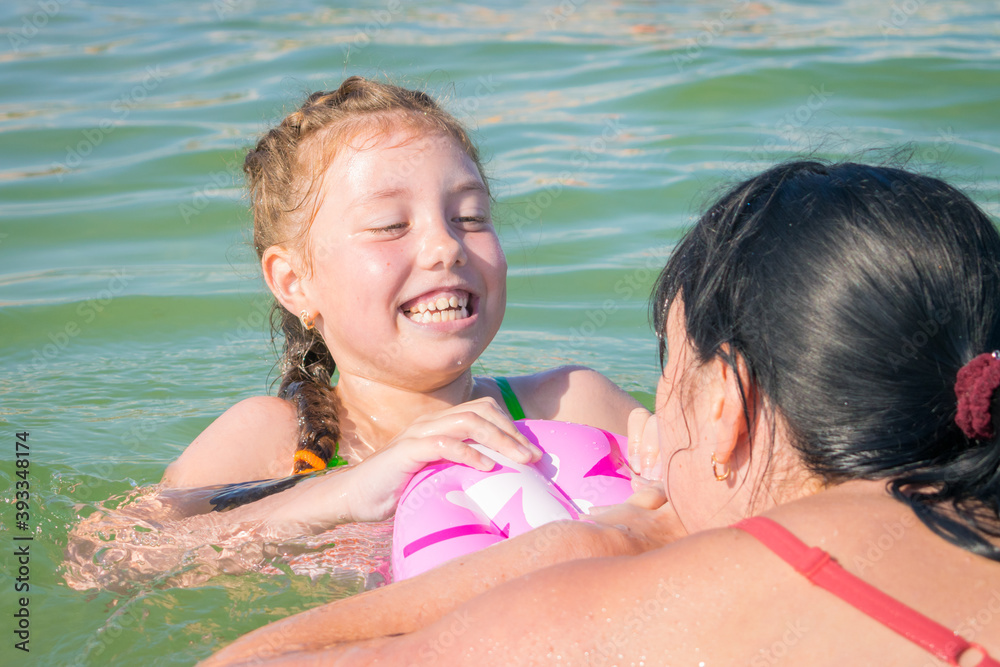 Fototapeta premium Mom and daughter are having fun at sea. A woman teaches a child to swim. Active family recreation on the water.