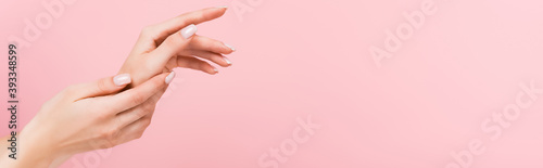partial view of woman applying cosmetic cream on hands isolated on pink  banner