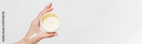 partial view of woman holding container with cosmetic cream isolated on white, banner