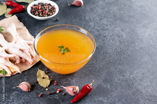 Glass plate with yellow bone broth on dark gray background. Healthy low-calories food is rich in vitamins, collagen and anti-inflammatory amino acids. Top view. Copy space.