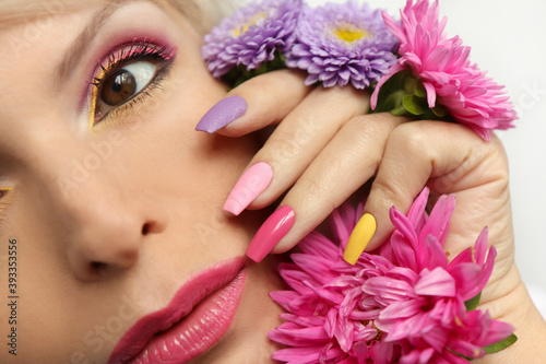 Fashionable multi-colored makeup and manicure on long nails of a girl with asters .