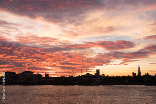 Cityscape of London during Autumn with a orange blue red purple skyline showing the city in black dark silhouette and also the river thames showing