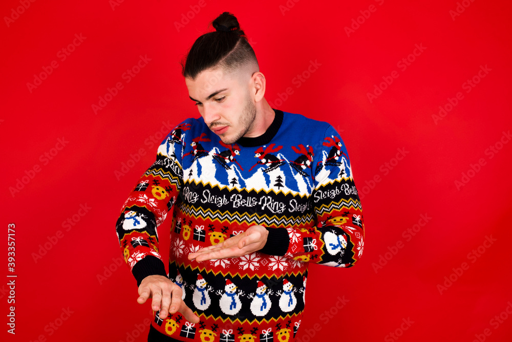 Young handsome Caucasian man wearing Christmas sweater against red wall, In hurry pointing to watch time, impatience, upset and angry for deadline delay. Young handsome Caucasian man wearing Christmas sweater against red wall, In hurry pointing to watch time, impatience, upset and angry for deadline delay.