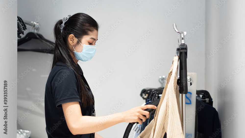 Female shop worker wearing face mask ironing cloth in the retail shop. Female shop worker wearing face mask ironing cloth in the retail shop.