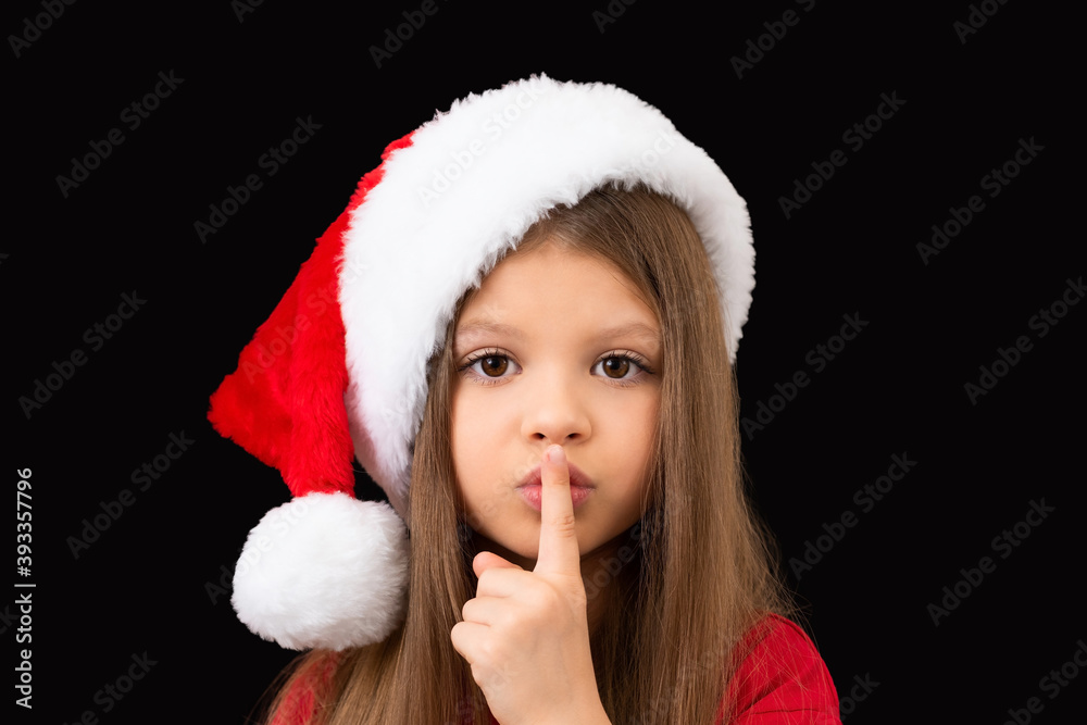A child in a Christmas hat holds a finger near his lips. A child in a Christmas hat holds a finger near his lips.