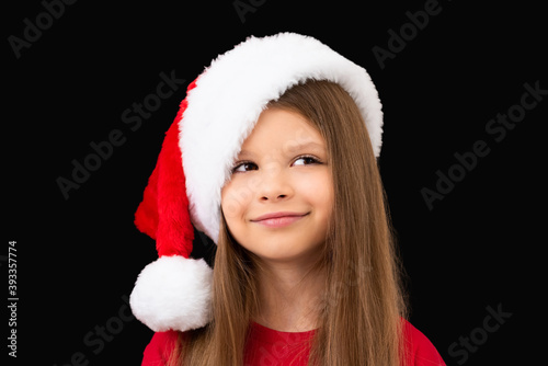 A cute little girl in a Christmas hat is smiling.