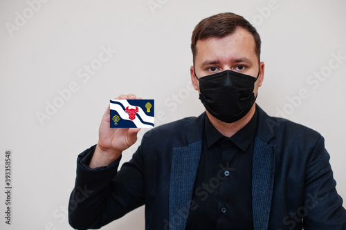 Man wear black formal and protect face mask, hold Oxfordshire flag card isolated on white background. United Kingdom counties of England coronavirus Covid concept. photo