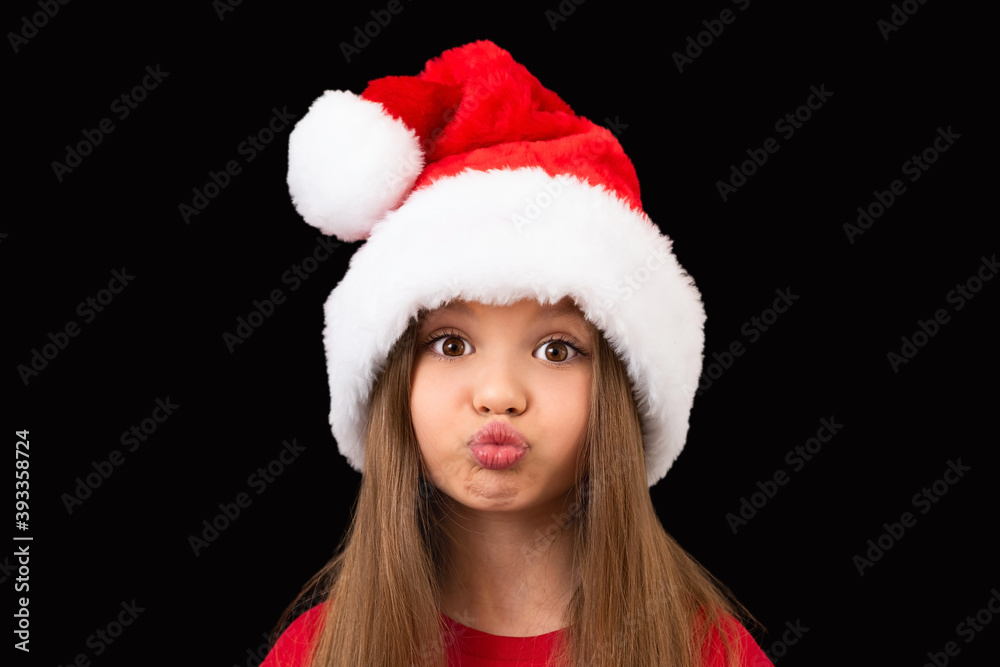 A little beautiful girl in a red Christmas hat poses. A little beautiful girl in a red Christmas hat poses.