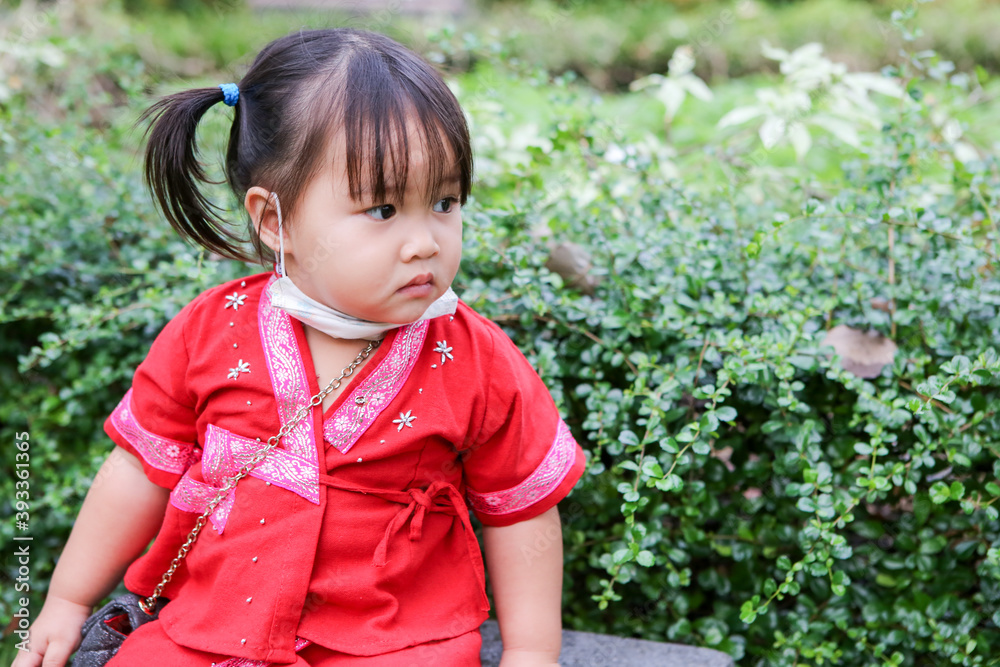 A cute Asian girl wearing a red hill tribe costume, wearing a mask in the playground A cute Asian girl wearing a red hill tribe costume, wearing a mask in the playground