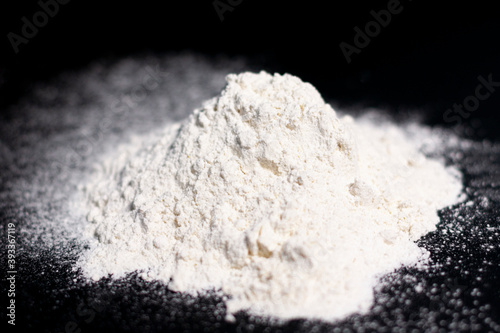 A mound of white flour on a dark surface. Top view.