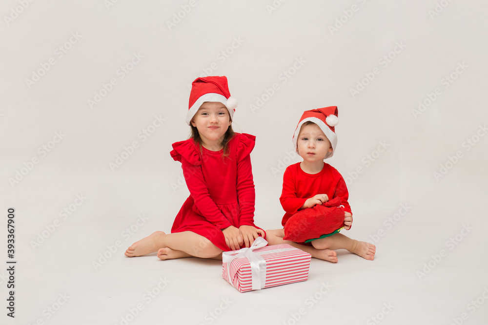 Obraz premium little brother and sister in Christmas costumes with caps with gifts on a white background
