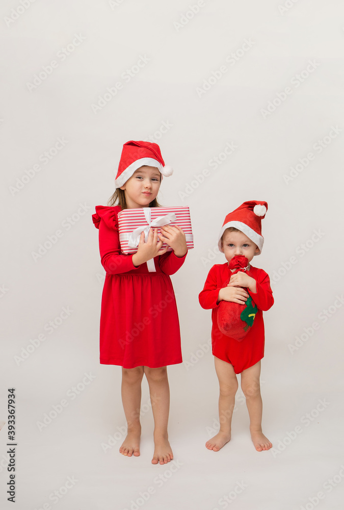 Obraz premium little brother and sister in Christmas costumes with caps with gifts on a white background